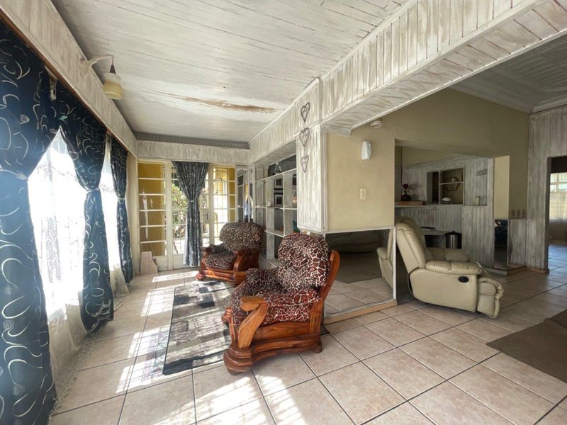 Spacious living area featuring tiled floors, timber-clad ceilings, and built-in shelving, offering a bright layout with direct access to the exterior through french doors.