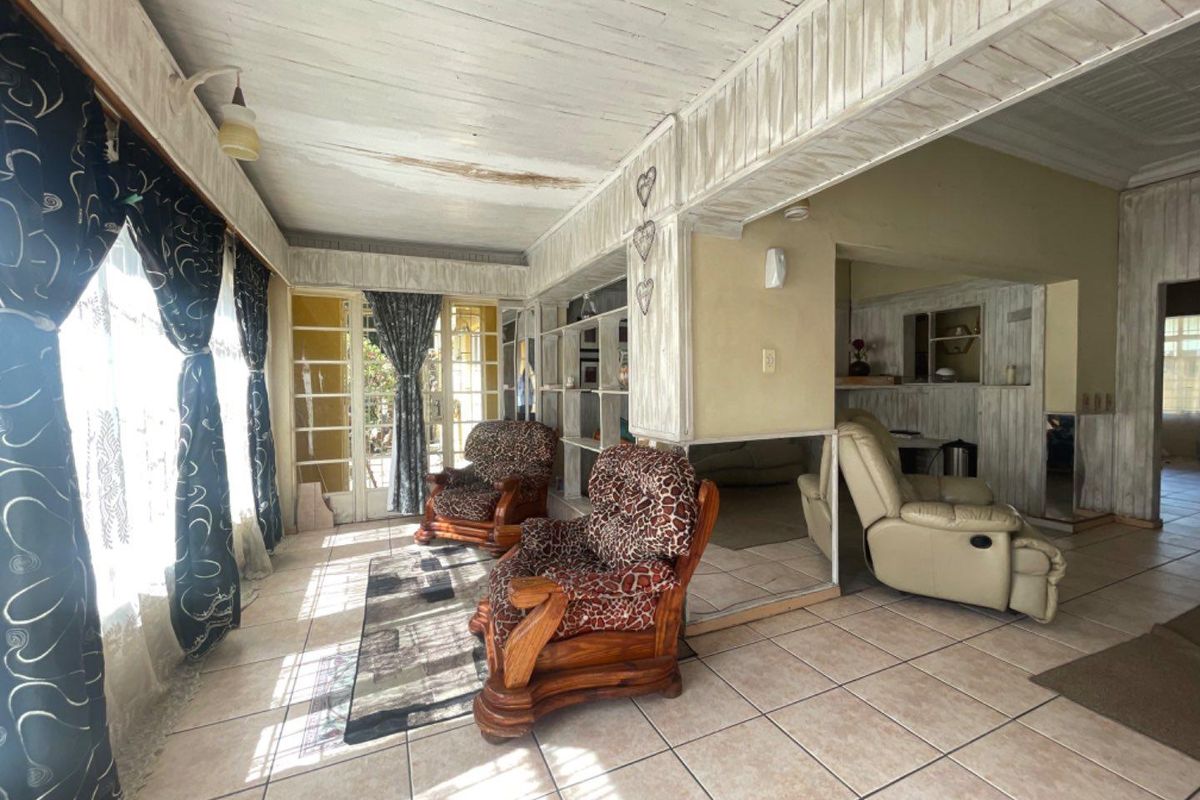 Spacious living area featuring tiled floors, timber-clad ceilings, and built-in shelving, offering a bright layout with direct access to the exterior through french doors.
