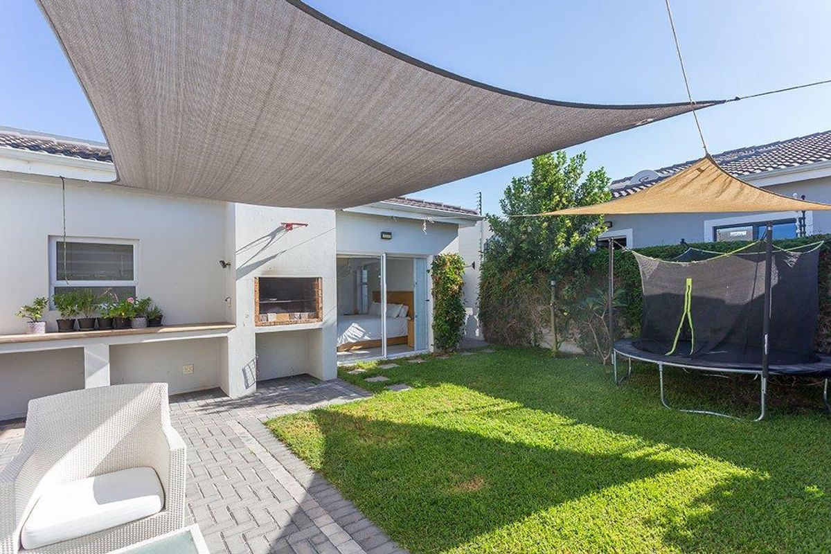 A well-maintained rear garden featuring a paved patio area with a built-in braai, shade sails, and a neat lawn.