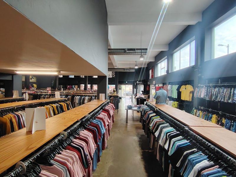 Spacious retail floor featuring polished concrete flooring, exposed industrial ducting, and extensive built-in clothing display racks with ample natural light from large windows.