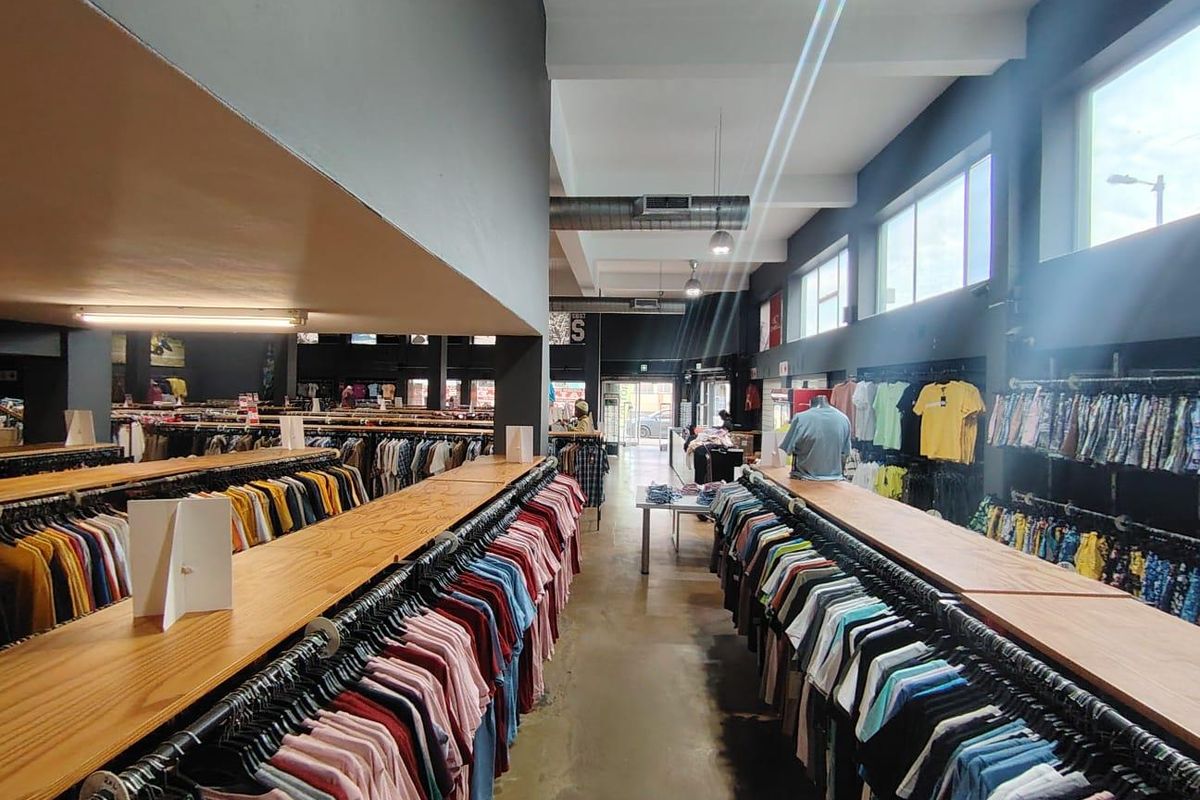 Spacious retail floor featuring polished concrete flooring, exposed industrial ducting, and extensive built-in clothing display racks with ample natural light from large windows.