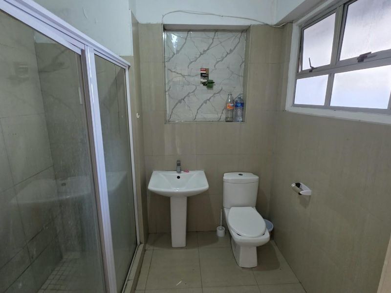 A functional bathroom featuring a pedestal basin, toilet, and a glass-enclosed shower with neutral wall and floor tiling.