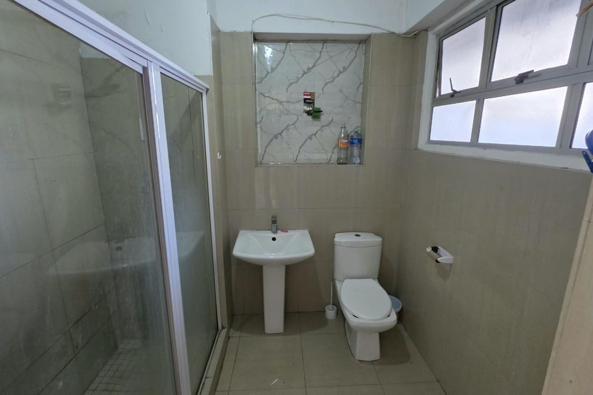 A functional bathroom featuring a pedestal basin, toilet, and a glass-enclosed shower with neutral wall and floor tiling.