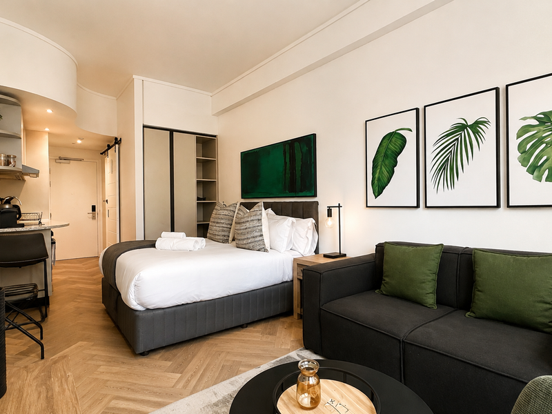 Modern open-plan studio apartment featuring herringbone timber flooring, a compact kitchenette, and a built-in wardrobe with a functional living and sleeping area.