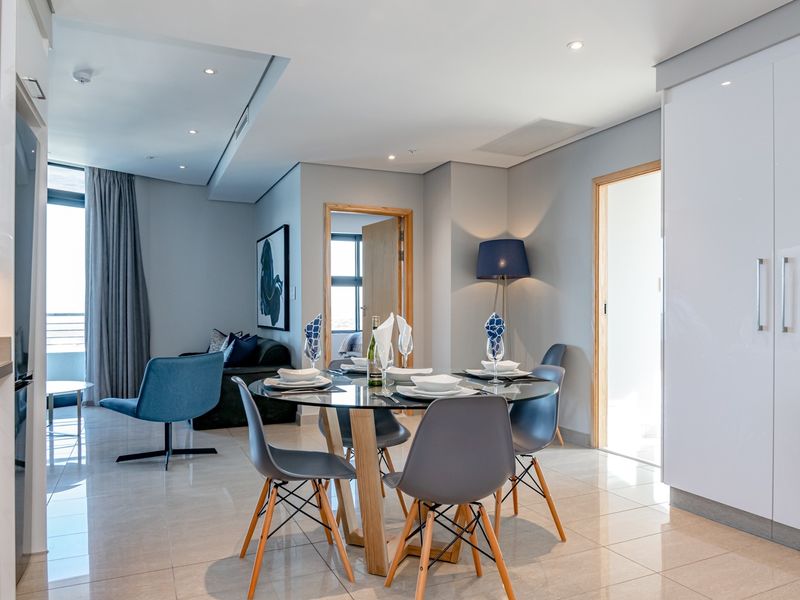 A modern open-plan living and dining area featuring sleek tiled floors, recessed lighting, and high-gloss built-in cabinetry.
