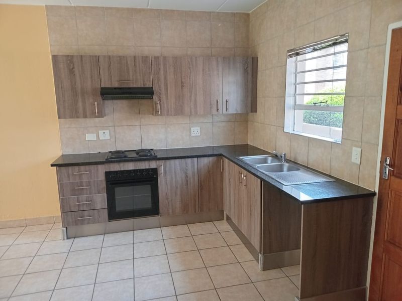 A clean and functional kitchen featuring wood-look laminate cabinetry, granite countertops, built-in oven, electric hob, and a double bowl sink with tiled splashbacks.