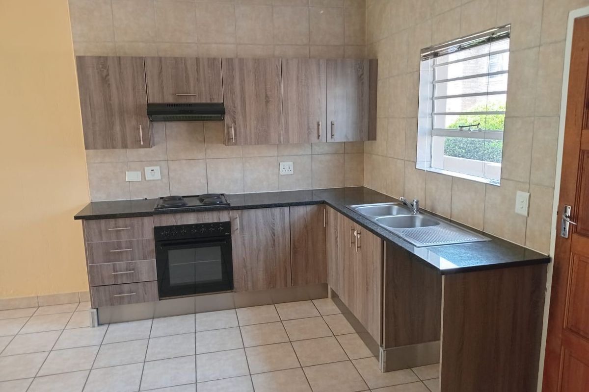 A clean and functional kitchen featuring wood-look laminate cabinetry, granite countertops, built-in oven, electric hob, and a double bowl sink with tiled splashbacks.