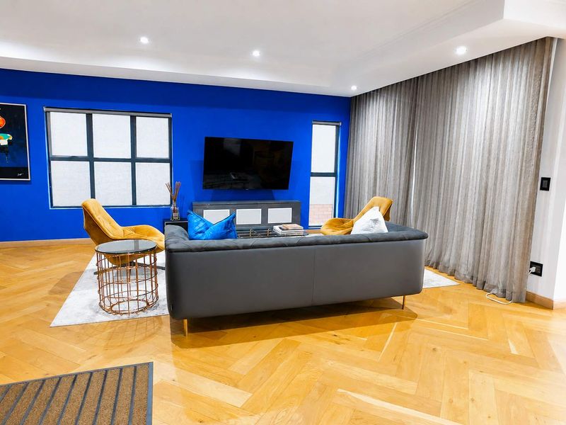 Modern living room featuring high-quality herringbone hardwood flooring, recessed ceiling lighting, and large windows with elegant full-length curtains.