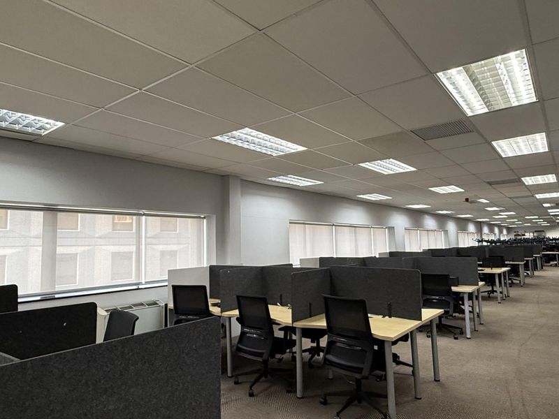 Spacious open-plan office area featuring suspended ceilings, recessed lighting, large windows with roller blinds, and carpeted flooring throughout.