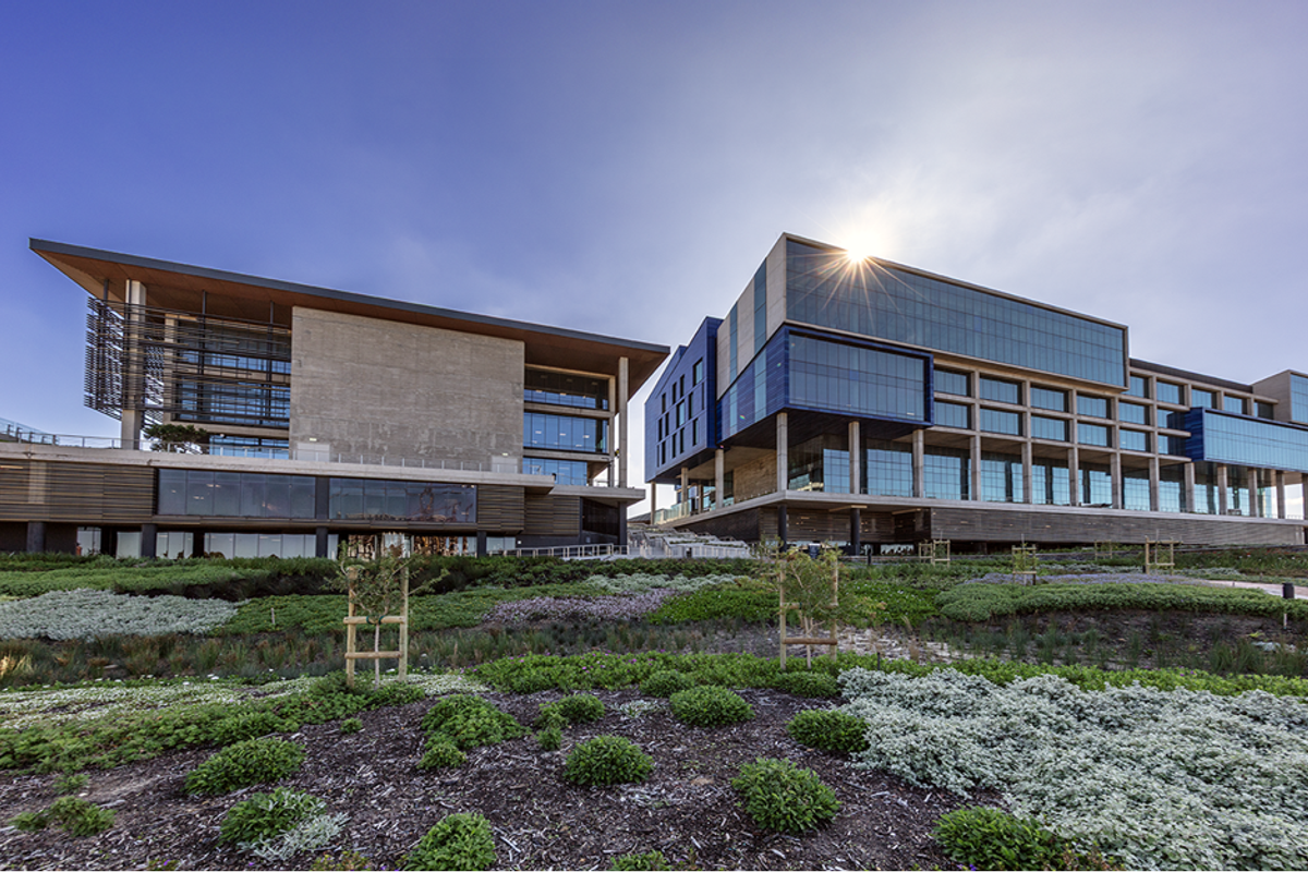 Modern office complex featuring contemporary glass and concrete architecture, set against a professionally landscaped garden area.