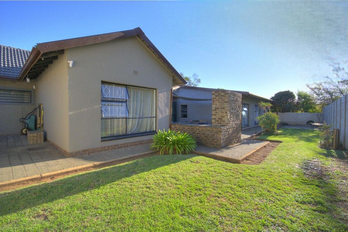 Rear view of the property featuring a paved patio area with a built-in brick braai, overlooking a private garden with boundary walling.