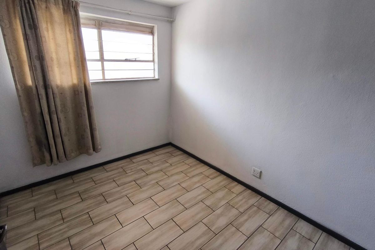 A compact, empty bedroom featuring neutral tiled flooring, a single window with curtain, and plain white walls, ready for personalization.