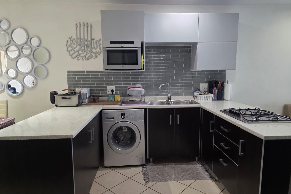 Modern kitchen featuring dark cabinetry, light quartz countertops, subway tile backsplash, built-in microwave, and a gas hob with integrated laundry appliance space.