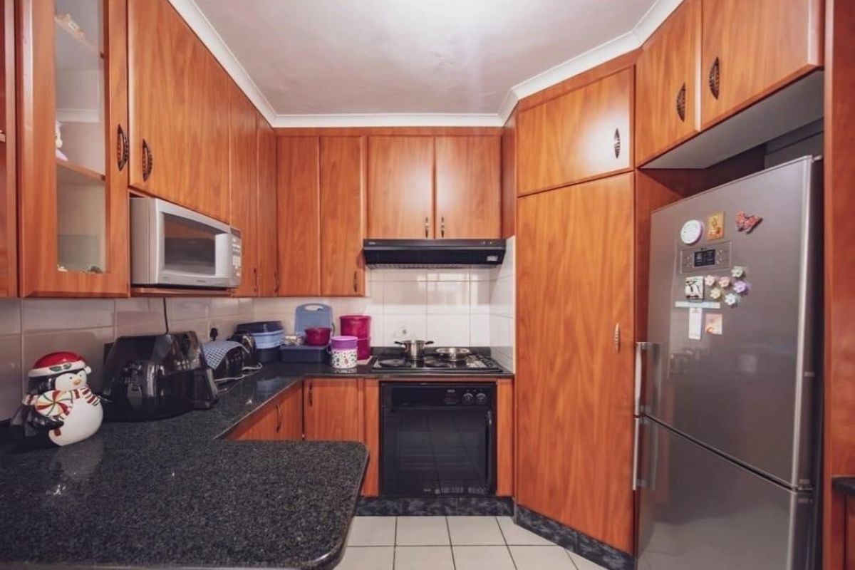 A functional kitchen featuring wood-look laminate cabinetry, granite countertops, built-in oven, gas hob, and tiled finishes throughout.