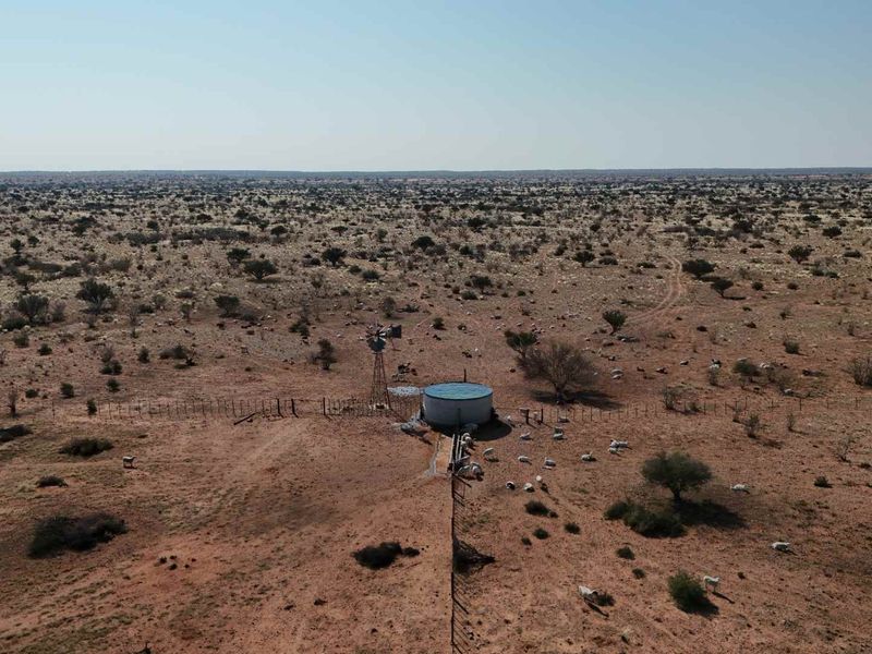 Aerial view of the farm landscape featuring a functional windmill and water reservoir infrastructure set within the expansive arid terrain.