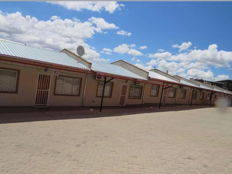 Exterior view of a row of townhouse units featuring paved driveway access, corrugated metal roofing, and security fixtures on windows and doors.