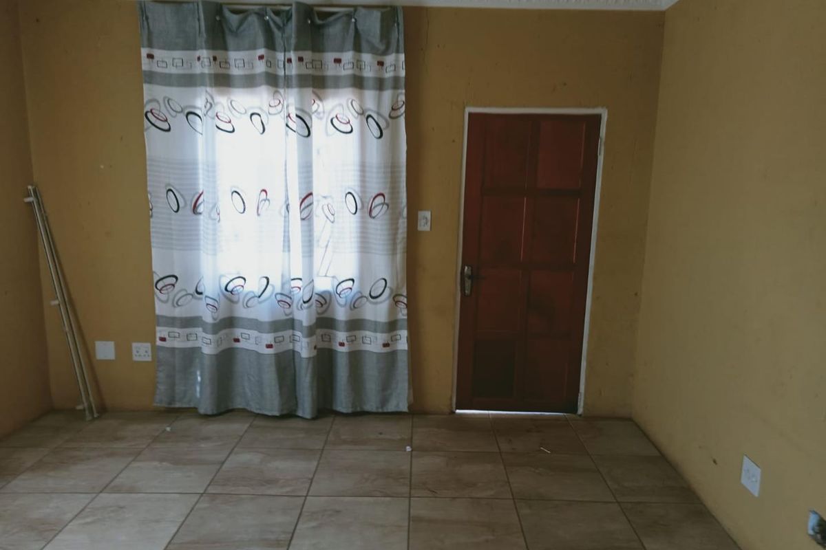 A simple, tiled living area featuring a wooden door and a window with curtains, offering a blank canvas for potential interior updates.