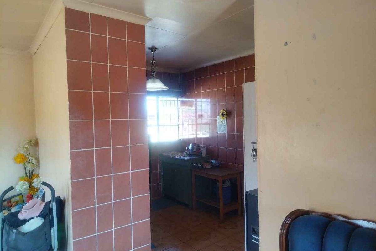 A view into a dated kitchen area featuring tiled walls and flooring, showing signs of wear and requiring cosmetic updates.