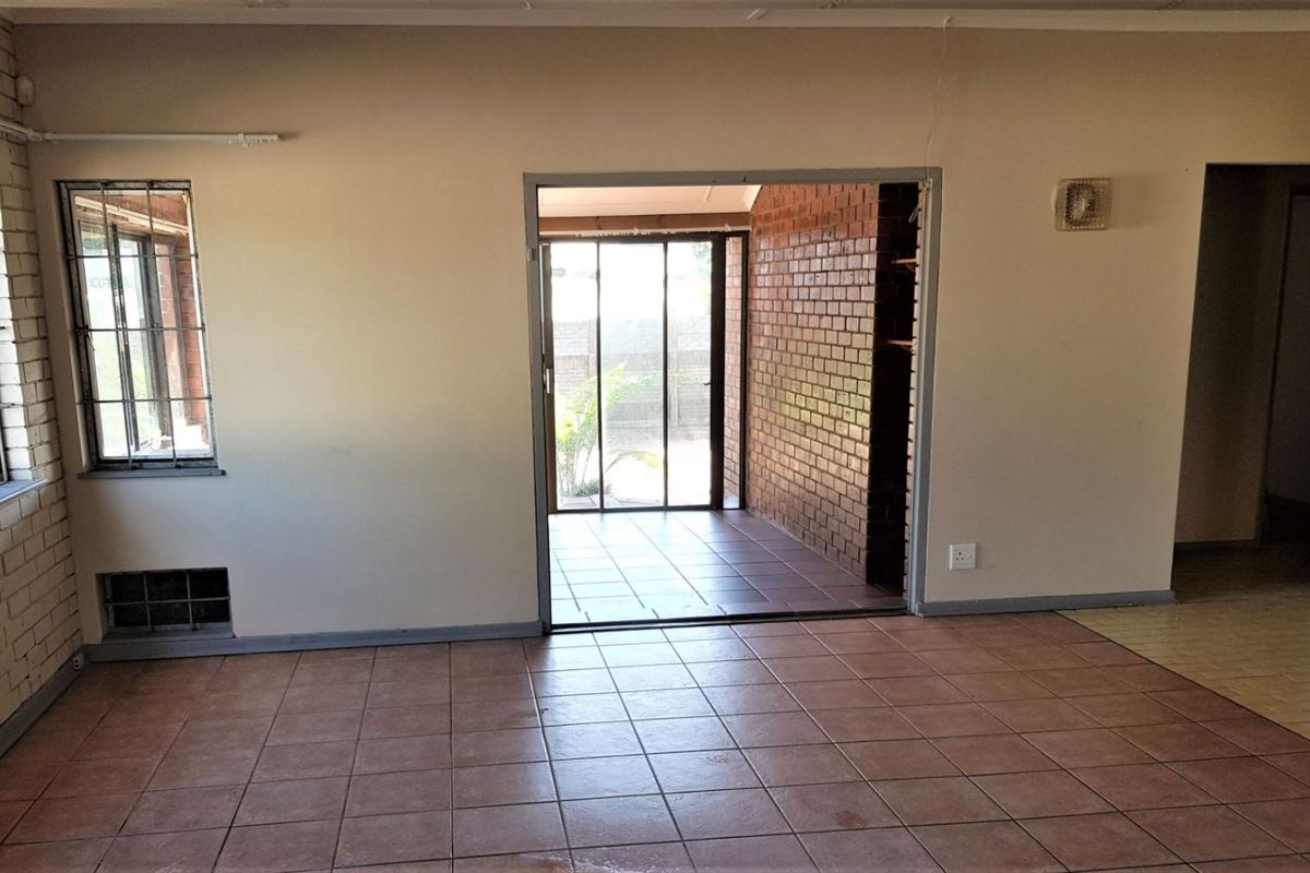 An empty living area featuring tiled floors, exposed brick accents, and a sliding glass door leading to an outdoor space.