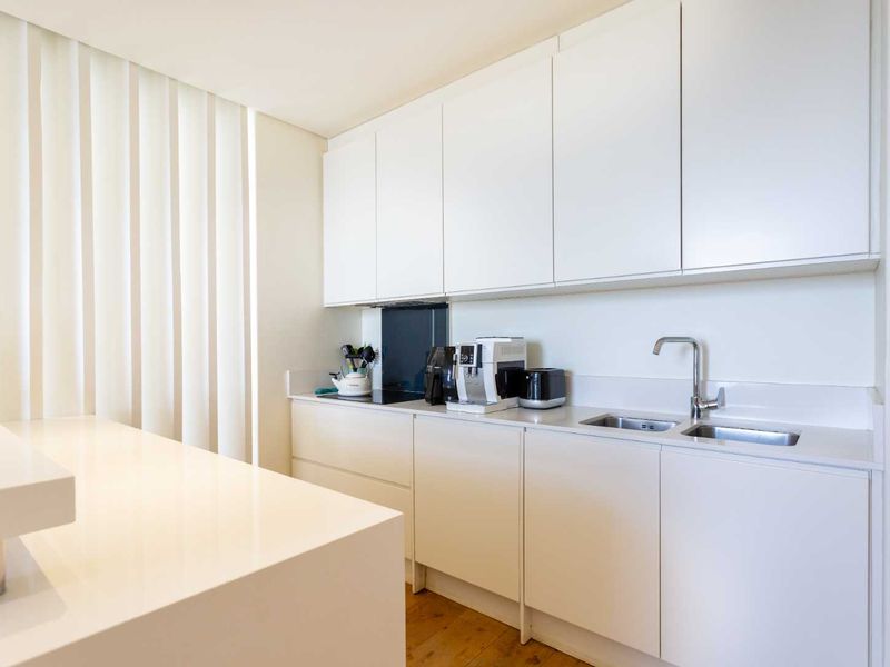 Modern minimalist kitchen featuring sleek white cabinetry, stone countertops, integrated hob, and a double sink with a contemporary mixer tap.