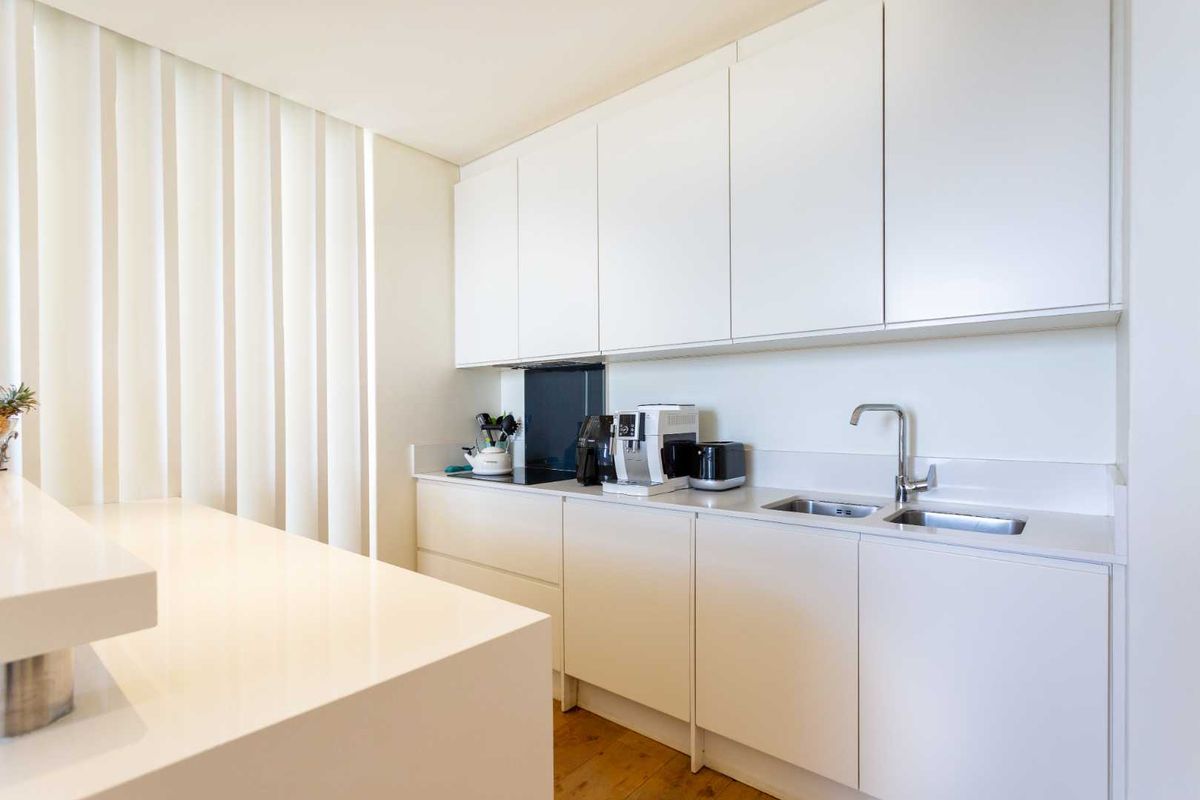 Modern minimalist kitchen featuring sleek white cabinetry, stone countertops, integrated hob, and a double sink with a contemporary mixer tap.