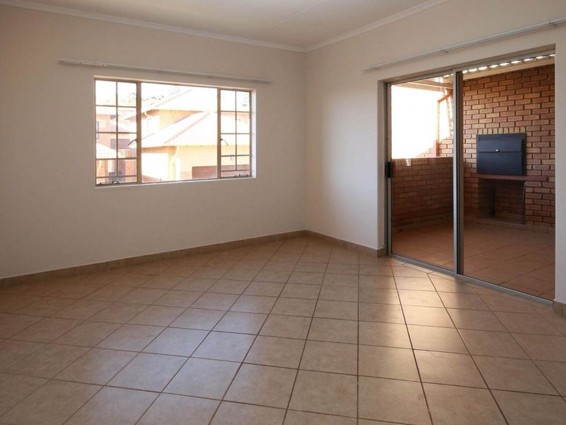 An empty living room featuring tiled flooring, large windows, and a sliding door leading to a patio with a built-in braai.
