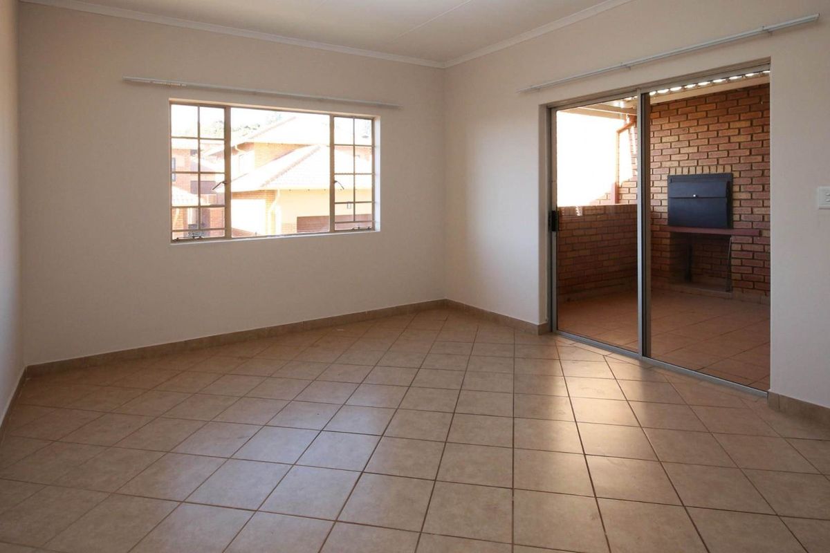 An empty living room featuring tiled flooring, large windows, and a sliding door leading to a patio with a built-in braai.