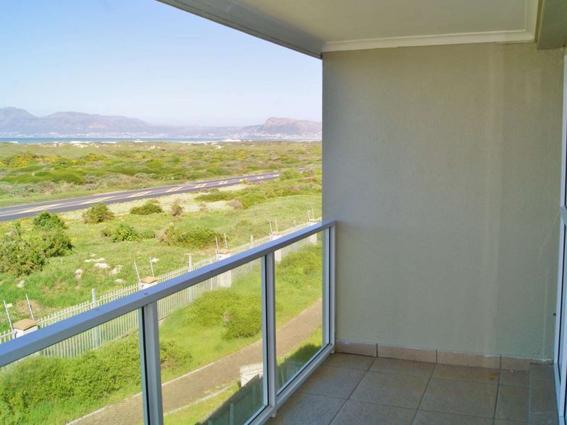 A clean, covered balcony featuring a glass balustrade and tiled flooring, offering expansive views of the surrounding landscape and coastline.