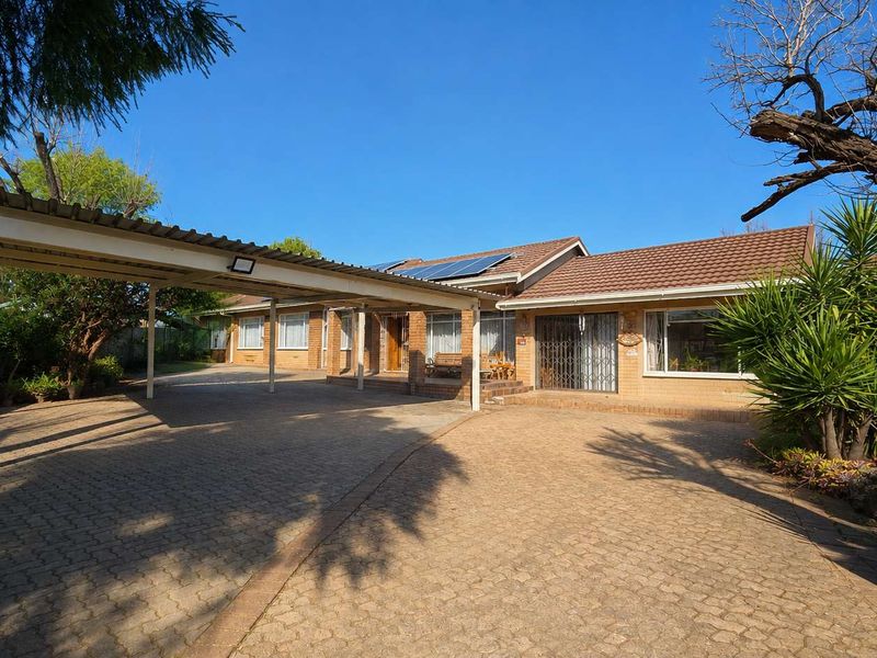 Front exterior view of a brick house featuring a large paved driveway, a covered carport, and solar panels installed on the tiled roof.