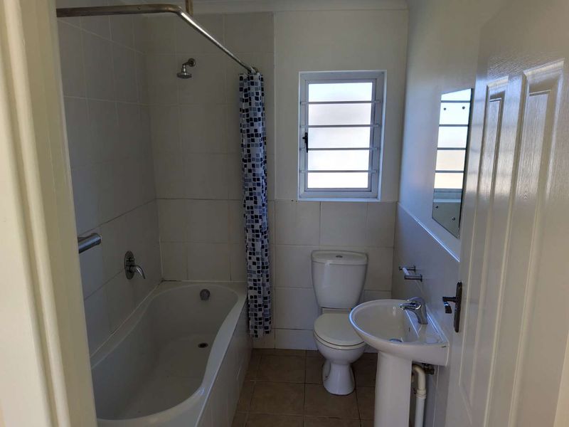 A functional bathroom featuring a bathtub with shower attachment, pedestal sink, and toilet, finished with tiled walls and flooring.