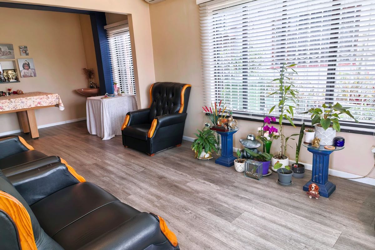A living room featuring wood-look laminate flooring, venetian blinds, and a wall-mounted air conditioning unit, with an adjacent alcove containing a small basin.