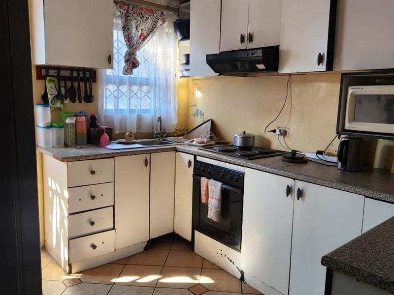 A compact kitchen featuring white cabinetry, laminate countertops, built-in oven, and tiled flooring, currently showing signs of wear and dated finishes.