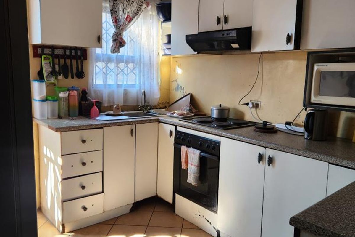A compact kitchen featuring white cabinetry, laminate countertops, built-in oven, and tiled flooring, currently showing signs of wear and dated finishes.