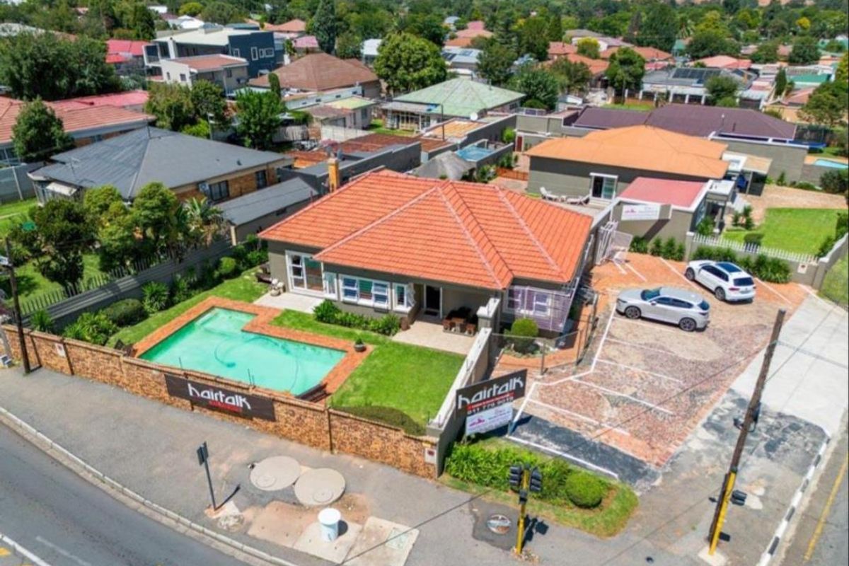 Aerial view of a residential property featuring a tiled roof, swimming pool, landscaped garden, and a paved parking area.