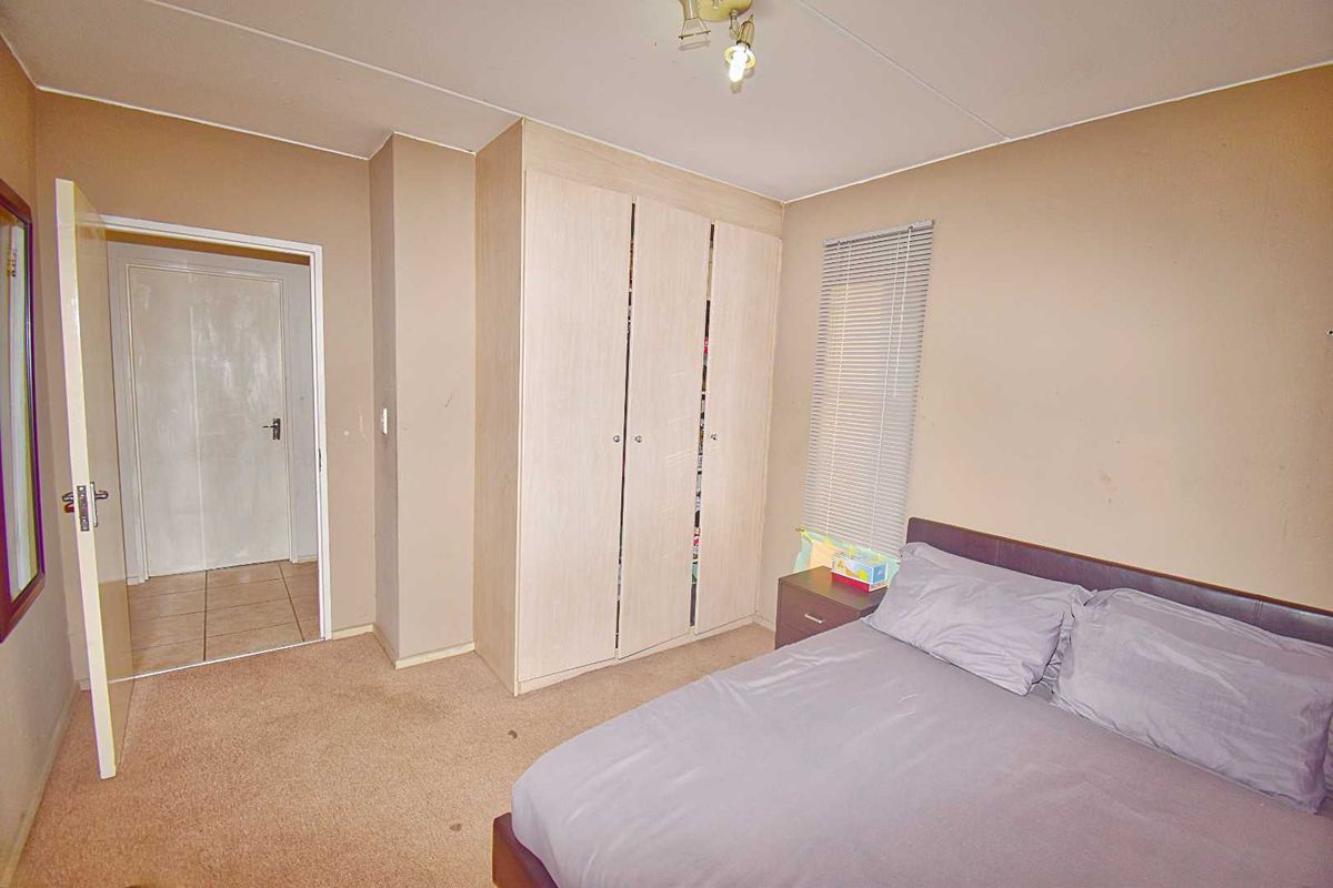 A bedroom featuring built-in wooden cupboards, neutral wall tones, and carpeted flooring, providing a functional and comfortable living space.