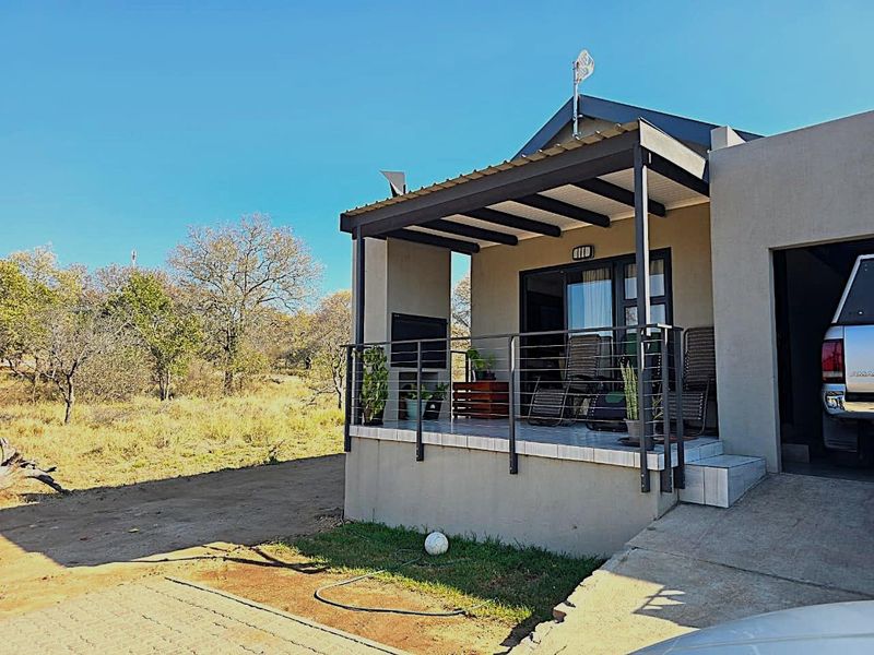 A covered outdoor patio featuring tiled flooring, a built-in braai, and metal railings, providing a functional space for outdoor living and entertaining.