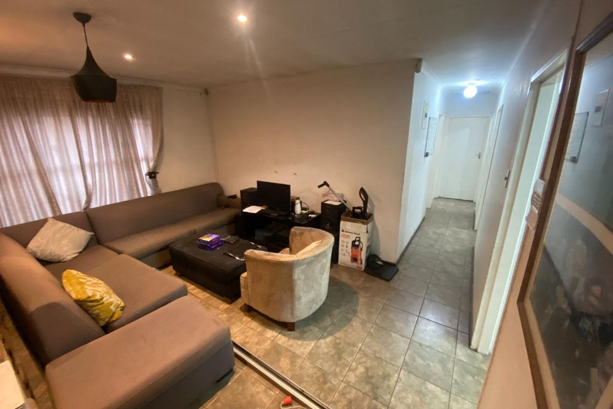 A living room area featuring tiled flooring and recessed ceiling lighting, leading into a hallway with access to other parts of the home.