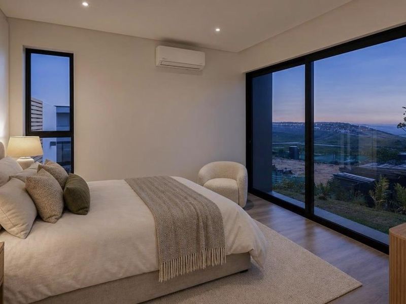 Modern bedroom featuring timber flooring, recessed lighting, split-system air conditioning, and large sliding glass doors offering expansive views.