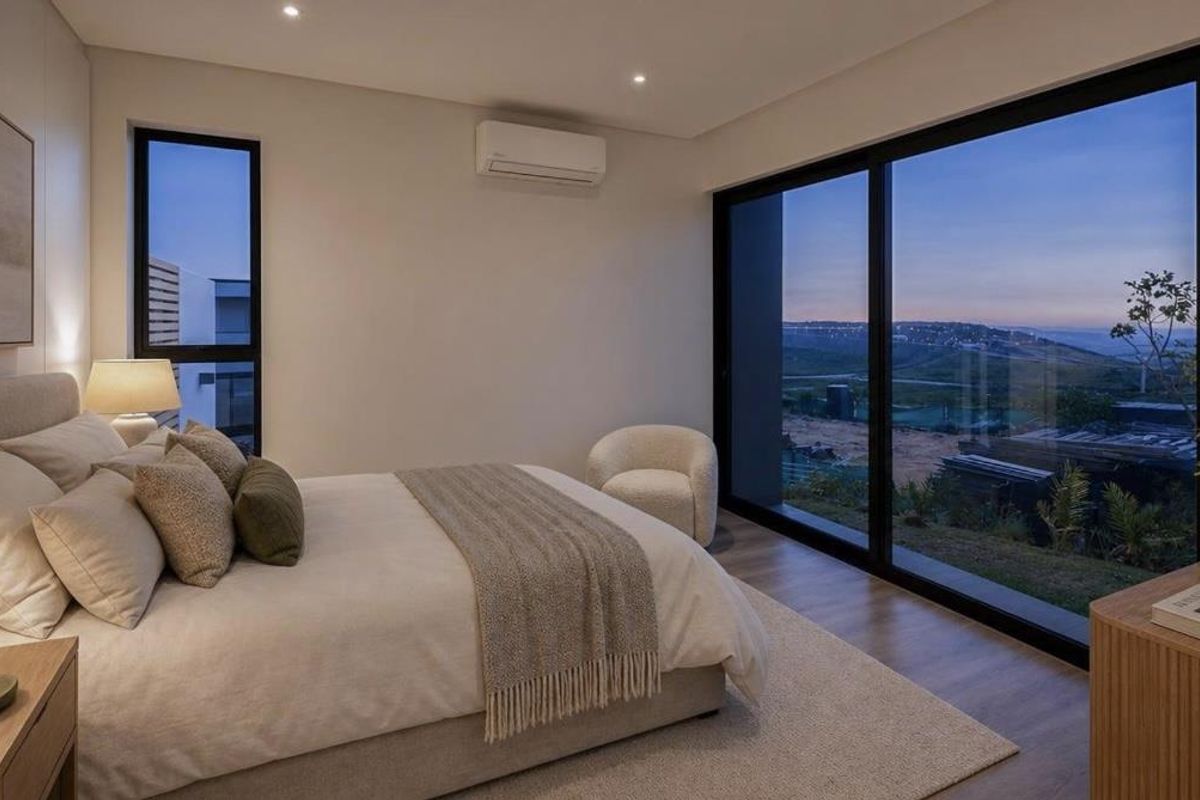 Modern bedroom featuring timber flooring, recessed lighting, split-system air conditioning, and large sliding glass doors offering expansive views.