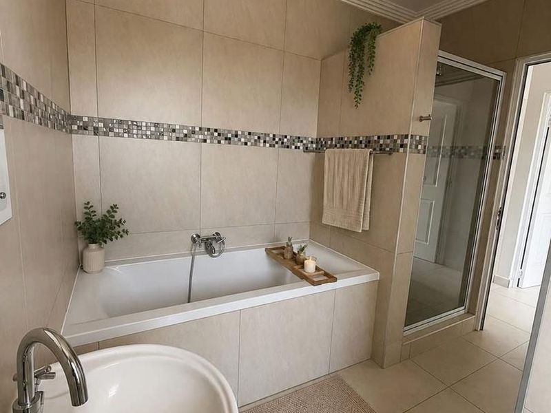 A well-maintained bathroom featuring a built-in bathtub, separate shower enclosure, and pedestal basin with neutral wall and floor tiling.