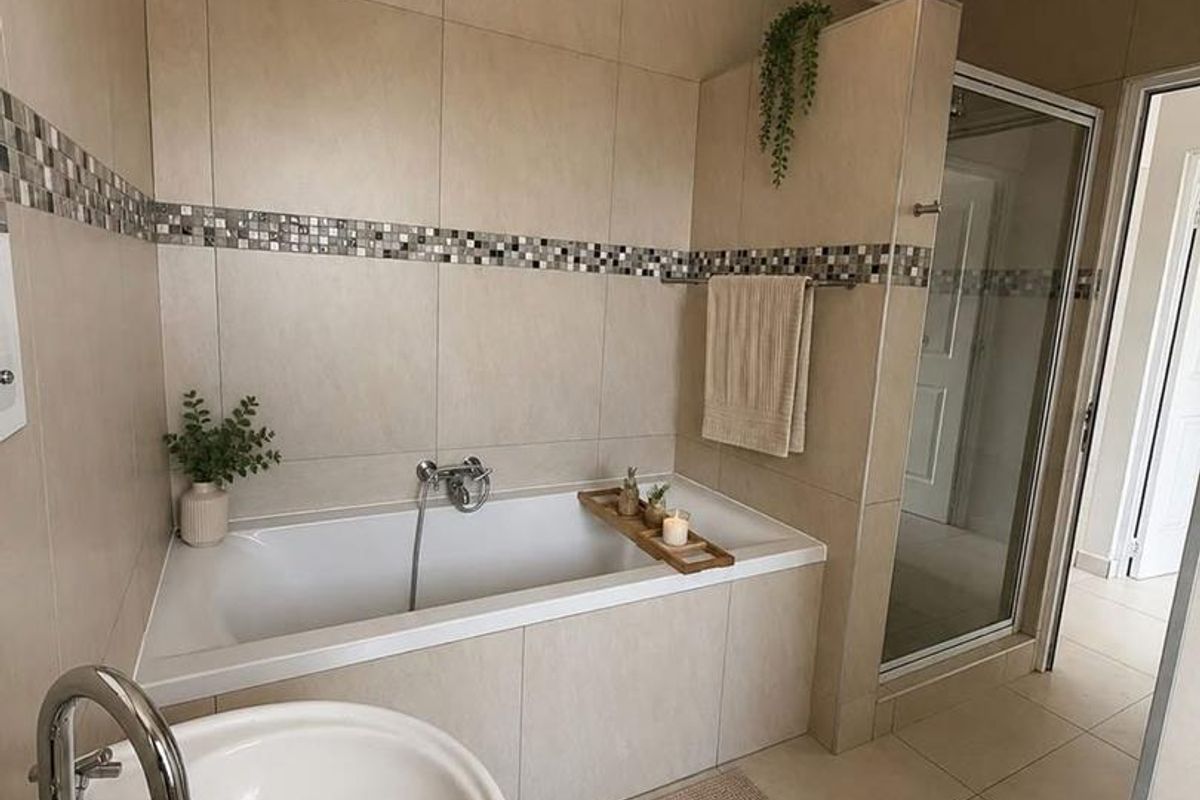 A well-maintained bathroom featuring a built-in bathtub, separate shower enclosure, and pedestal basin with neutral wall and floor tiling.