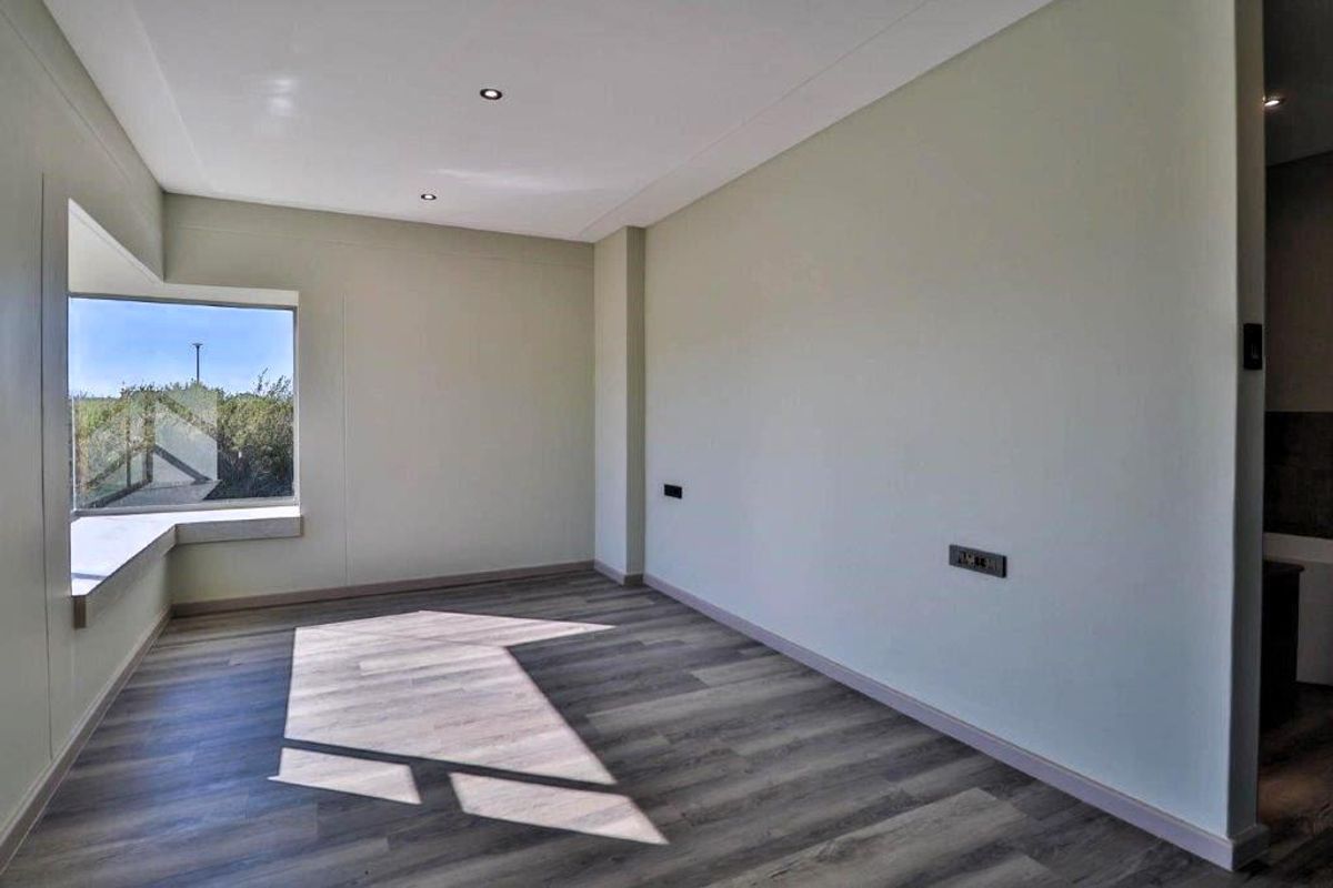 A bright, empty bedroom featuring modern laminate flooring, recessed downlighting, and a large window with a built-in sill.
