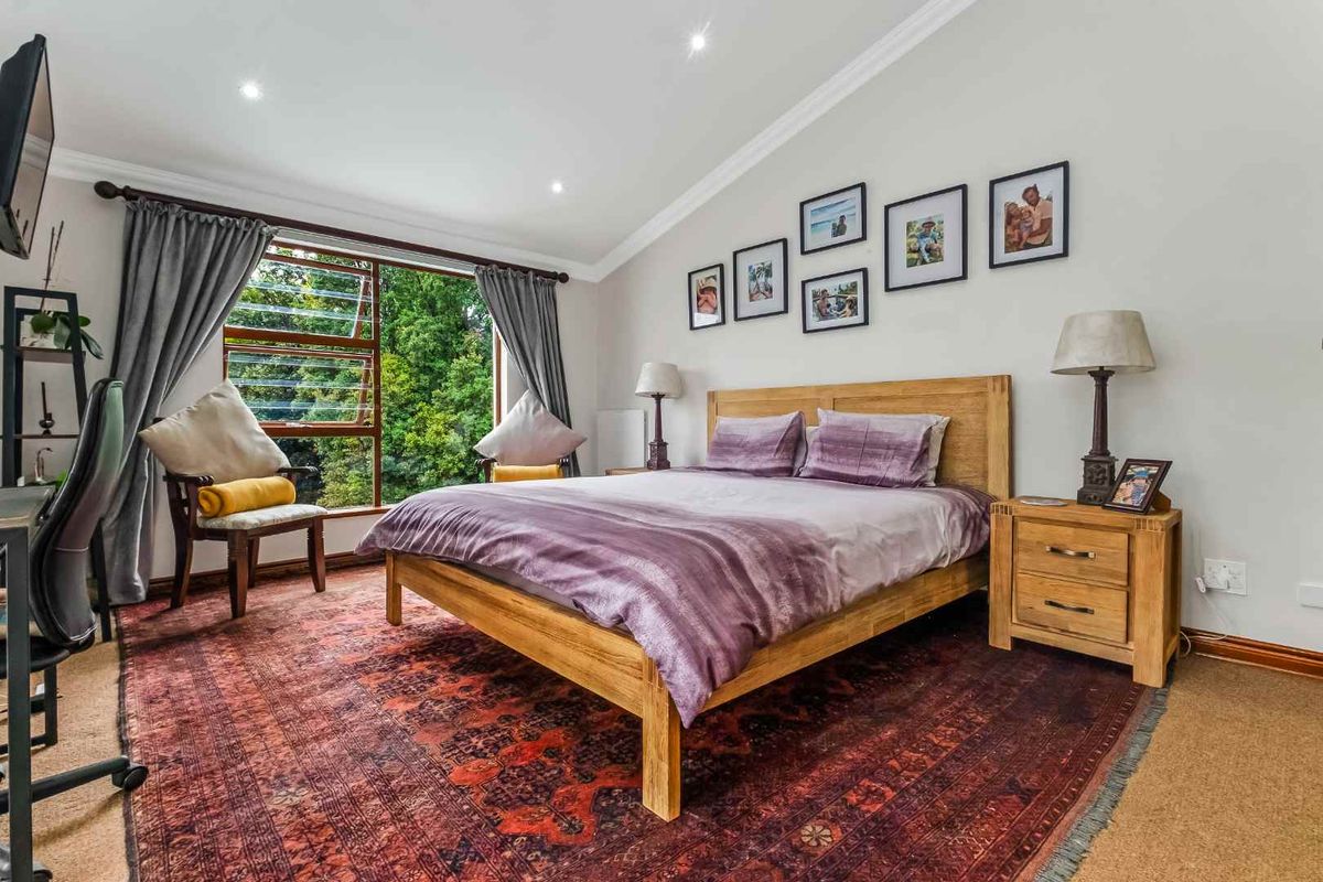 A well-maintained bedroom featuring large windows with garden views, recessed ceiling lighting, and neutral wall finishes.