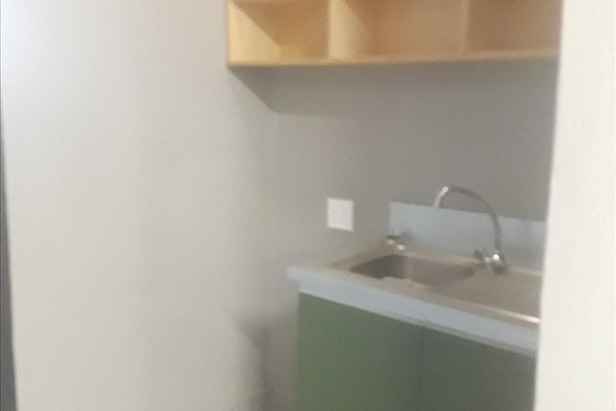 A functional scullery area featuring a stainless steel sink, built-in base cabinetry, and wall-mounted open shelving for storage.