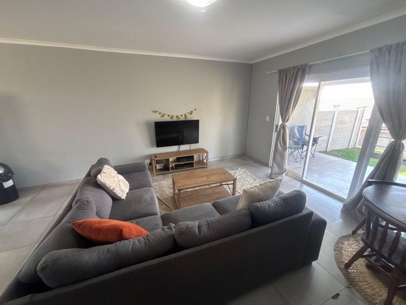 A bright living room featuring tiled flooring and a large sliding glass door providing direct access to the outdoor patio area.