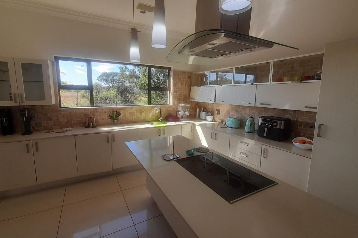 Modern kitchen featuring white cabinetry, stone countertops, a central island with an integrated cooktop, and a glass extractor fan with scenic window views.