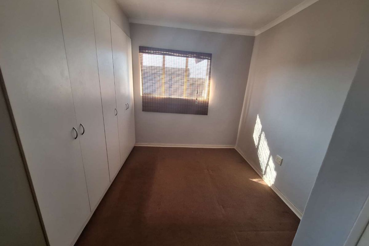 A clean, empty bedroom featuring built-in cupboards, carpeted flooring, and a window with fitted blinds, offering a neutral space ready for personalization.