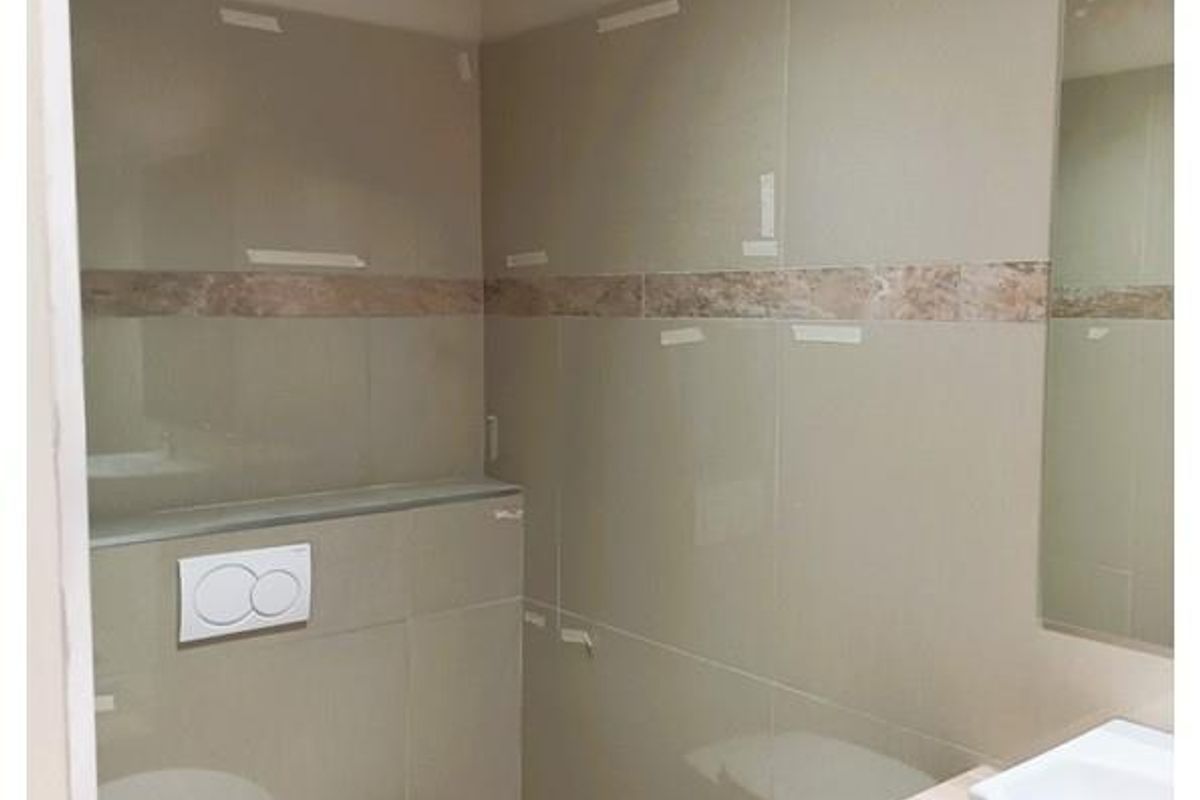 A modern bathroom featuring neutral wall tiles, a wall-mounted toilet with a concealed cistern, and a vanity basin.