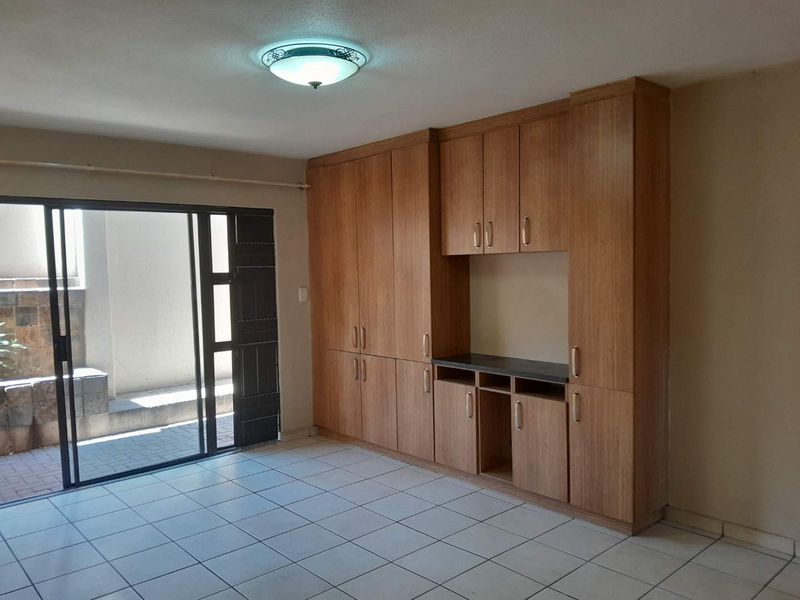 An empty living area featuring built-in wooden cabinetry, ceramic floor tiles, and a sliding glass door providing access to an outdoor patio space.
