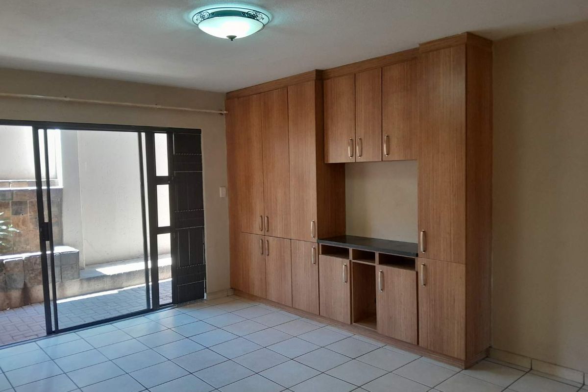An empty living area featuring built-in wooden cabinetry, ceramic floor tiles, and a sliding glass door providing access to an outdoor patio space.